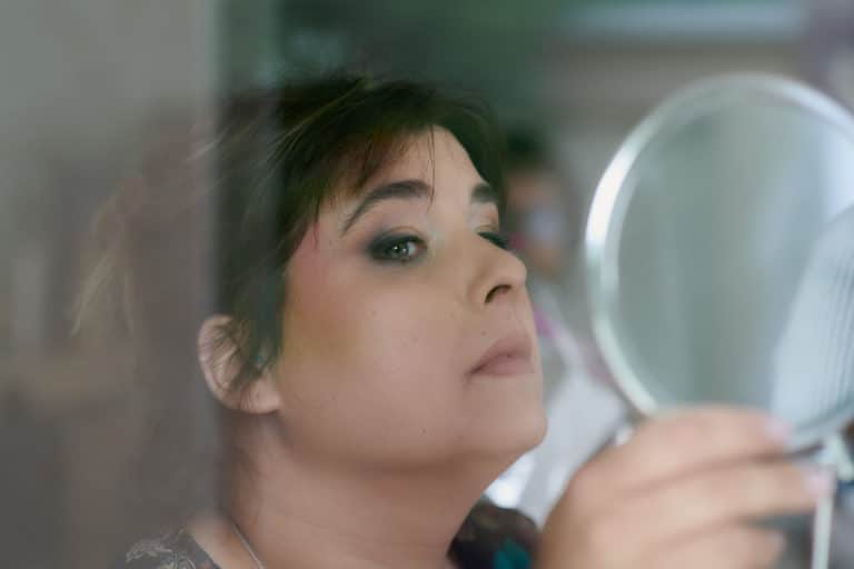 Les préparatifs avant le mariage : la future mariée regarde son maquillage dans un miroir.