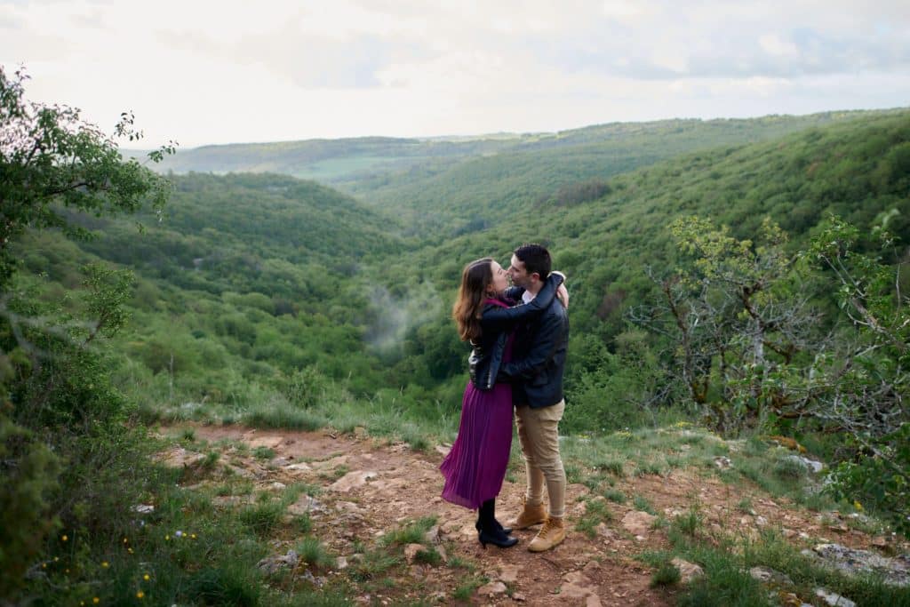 Séance couple au-dessus d'une falaise. Les deux amoureux s'embrassent devant une vue imprenable.