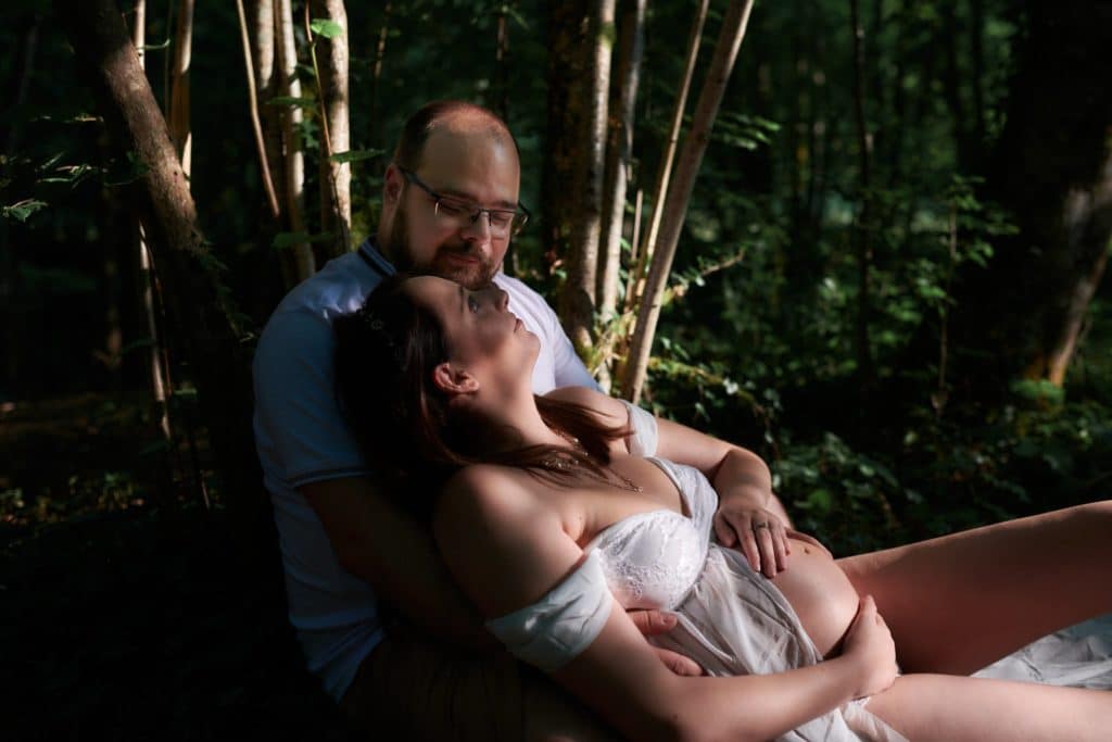 Une femme enceinte adossée sur son homme dans les bois, lors d'une séance grossesse.