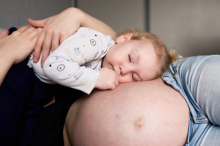 Moment de tendresse d'un bébé, la tête posée sur le ventre arrondi de sa maman, les yeux fermés, lors d'une séance grossesse