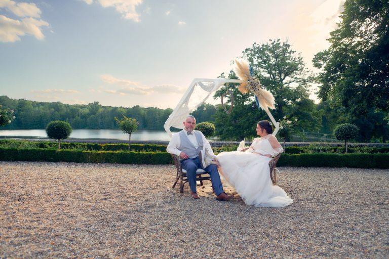 Photo fun d'un couple de mariés dont la mariée à poser ses jambes chaussées de baskets sur les cuisses de son mari. En arrière le plan, la rivière passant dans le domaine du Château de Verrerie à Oizon.
