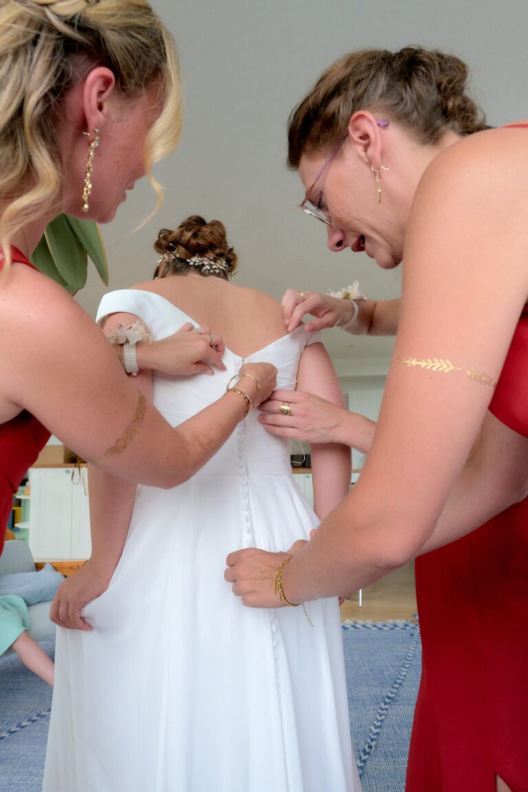 Les demoiselles d'honneur boutonnent la robe de la mariée.