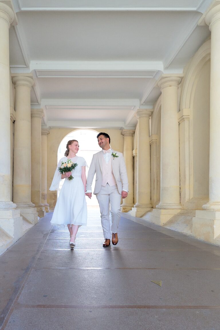 Couple de mariés traversant un porche main dans la main.